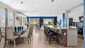 A modern kitchen with a central island, dining area with chairs, and a view of the outside.