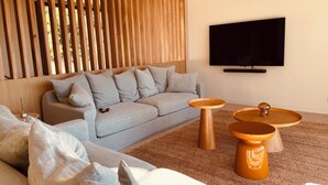A modern living room with a grey sofa, wooden slats, a TV, and two wooden side tables. - Villa l'Annexe between Avignon and Nîmes: outdoor swimming pool, gym,... (Rochefort-du-Gard)