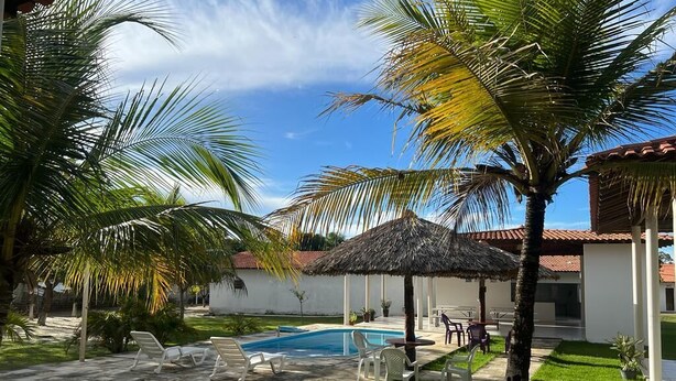 A pool area with lounge chairs, a thatched-roof gazebo, and palm trees. - Pousada Estrela da manhã (Barreirinhas)