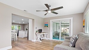 Un vaste espace de vie agrémenté d’un ventilateur de plafond, un coin repas avec une porte vitrée et une cuisine située à l’arrière-plan.