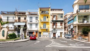 A street view with multi-story buildings, a red car parked on the side, and a clear blue sky. - Naxos Bay View With Terrace by Wonderful Italy (Giardini Naxos)