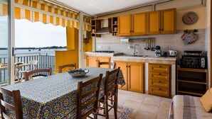 A kitchen with wooden cabinets, a dining table with chairs, a view of the sea, and a clock on the wall. - Naxos Bay View With Terrace by Wonderful Italy (Giardini Naxos)