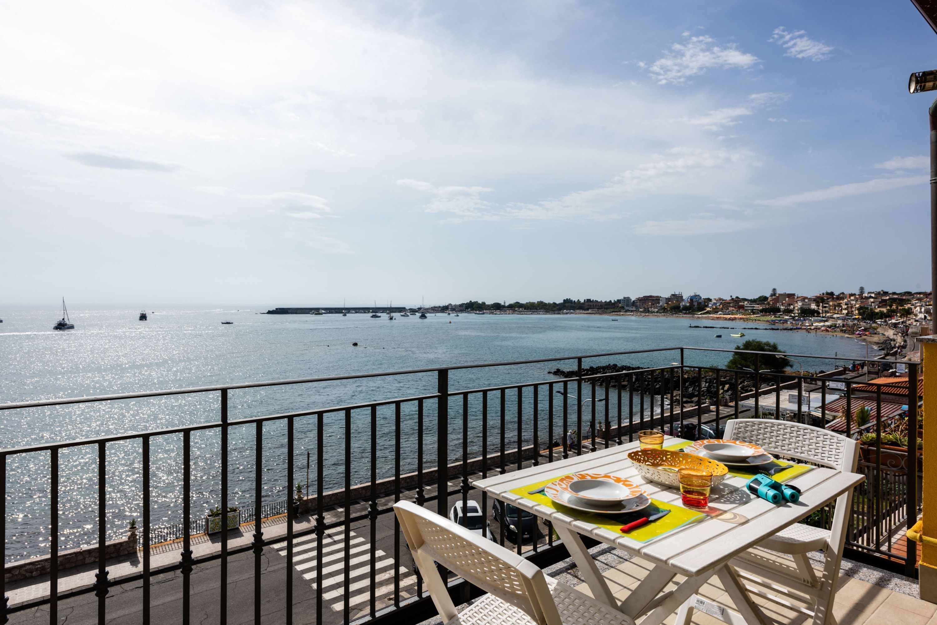 Un balcón con una mesa lista para comer, con vistas a una ciudad costera y barcos en el agua.