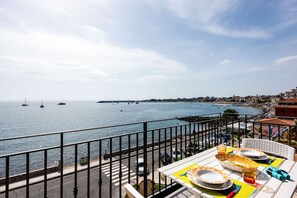 Un balcon avec une table dressée pour le dîner, offrant une vue sur une ville côtière et la mer.