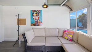 Ein modernes Wohnzimmer mit Sofa, einem Gemälde, einer Lampe und Blick ins Freie.