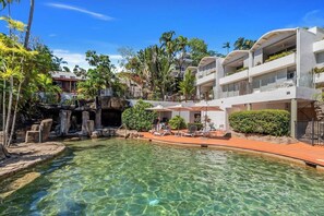 A pool area with clear water, lounge chairs, and a multi-story building with balconies.