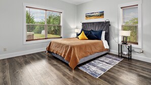 Ein Schlafzimmer mit einem Bett, Deckenventilator, Nachttisch, Lampe und großen Fenstern mit Jalousien.
