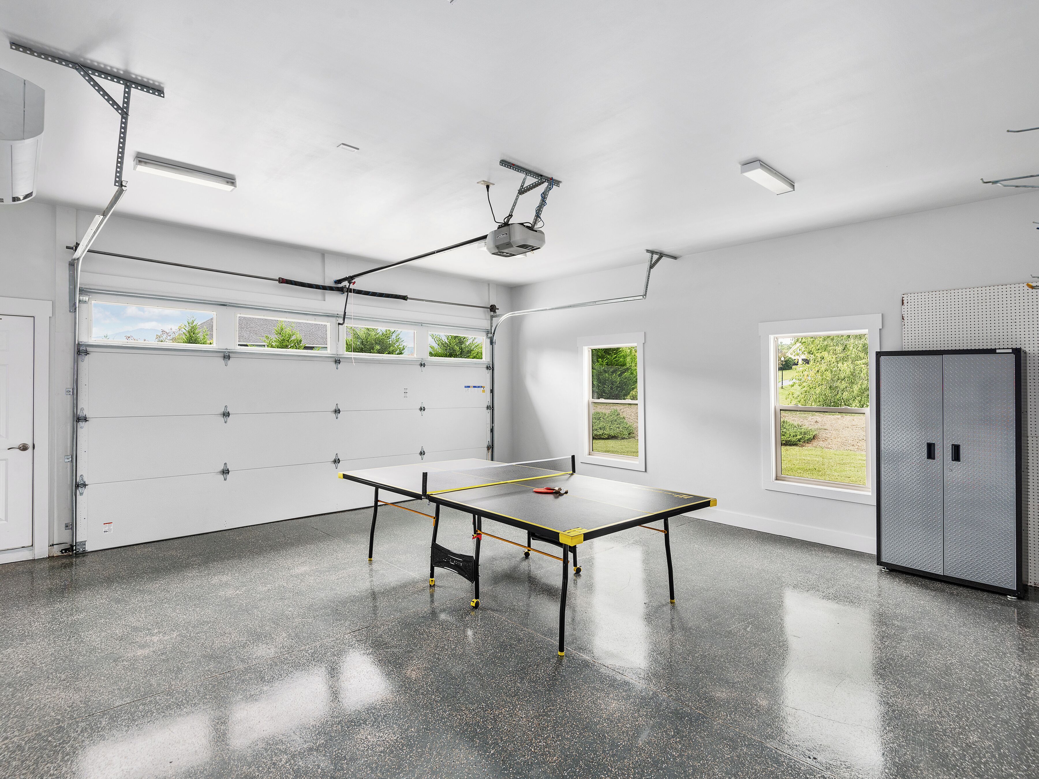 A garage with a ping pong table, a utility room, and a large window with a view of greenery.