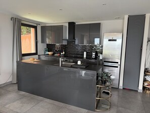 A modern kitchen with a central island, stainless steel appliances, and a black backsplash.