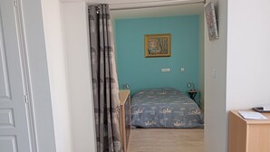 A bedroom with a bed, a desk, a chair, a nightstand, and a painting on the wall. - Cosy dwelling in the village center (Aubigné-Racan)