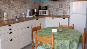 A kitchen with white cabinets, a wooden dining table with a green tablecloth, a black range hood, and a white refrigerator. - Cosy dwelling in the village center (Aubigné-Racan)