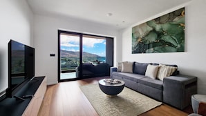 A modern living room with a large flat-screen TV, a grey sofa with patterned cushions, a round coffee table, and a large abstract painting on the wall. - Blissful Suite by LovelyStay (Funchal)