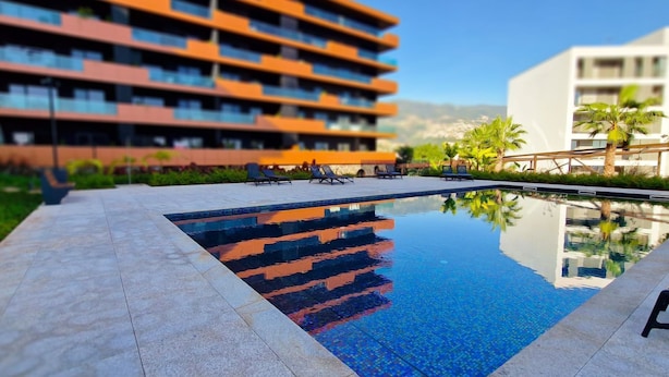 A swimming pool with lounge chairs, surrounded by a landscaped area with palm trees and a modern building in the background. - Blissful Suite by LovelyStay (Funchal)