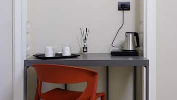 Una habitación pequeña y moderna con escritorio, una silla, un hervidor eléctrico y toma de corriente.