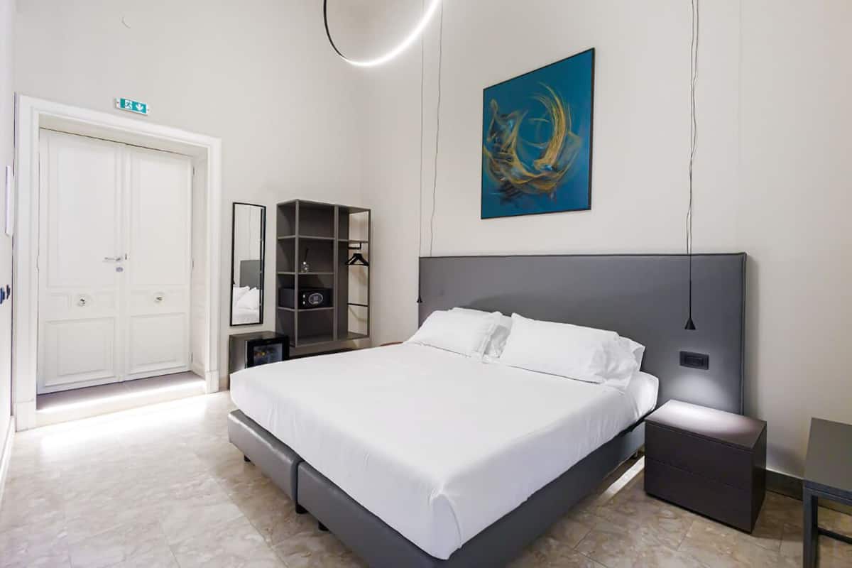 A modern bedroom with a large bed, a wardrobe, a bedside table, and a wall-mounted artwork.