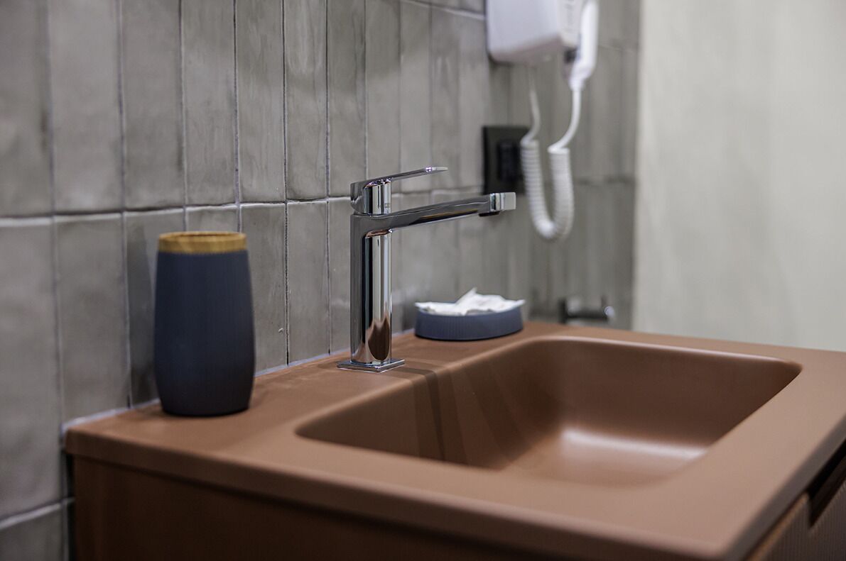 Een wastafel met een chromen kraan, een blauwe zeephouder en een witte handdoekdispenser aan de muur.