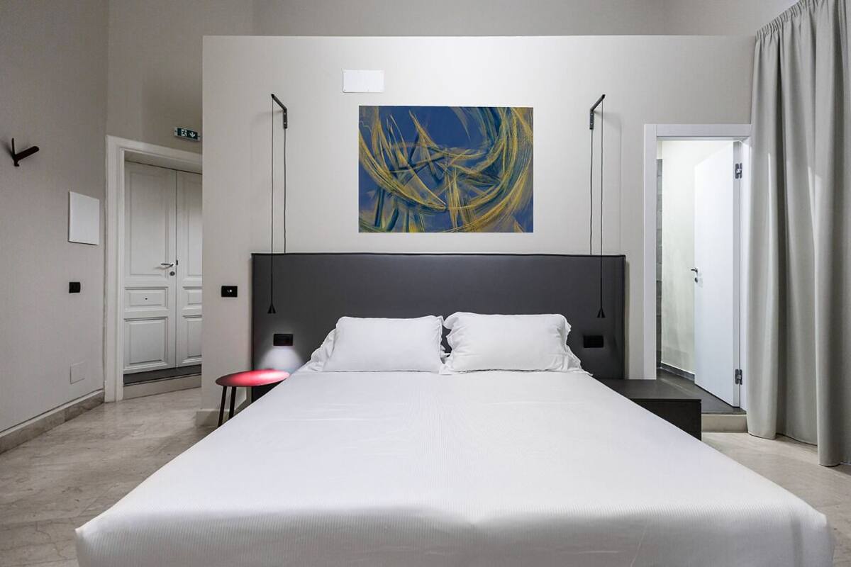 A modern hotel room with a large bed, a painting on the wall, and a view of the outside.
