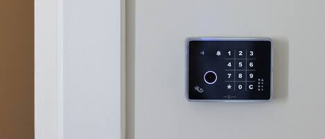 A wall-mounted electronic keypad, likely for a door lock, with a numeric keypad and a circular button.