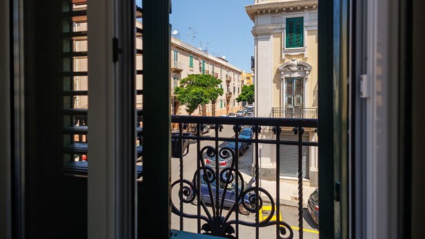 A balcony with a wrought iron railing overlooking a street with parked cars and buildings. - RV 2.0  (Messina)