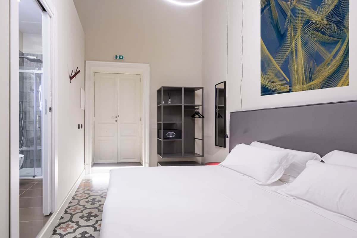 A hotel room with a bed, a wardrobe, a mirror, and a shower area.