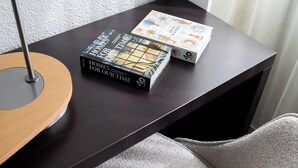 A dark wooden desk with a lamp, two books titled 'Homes for Our Time', and a grey chair. - Sweet Home By Novotel Bordeaux Mérignac (Mérignac)