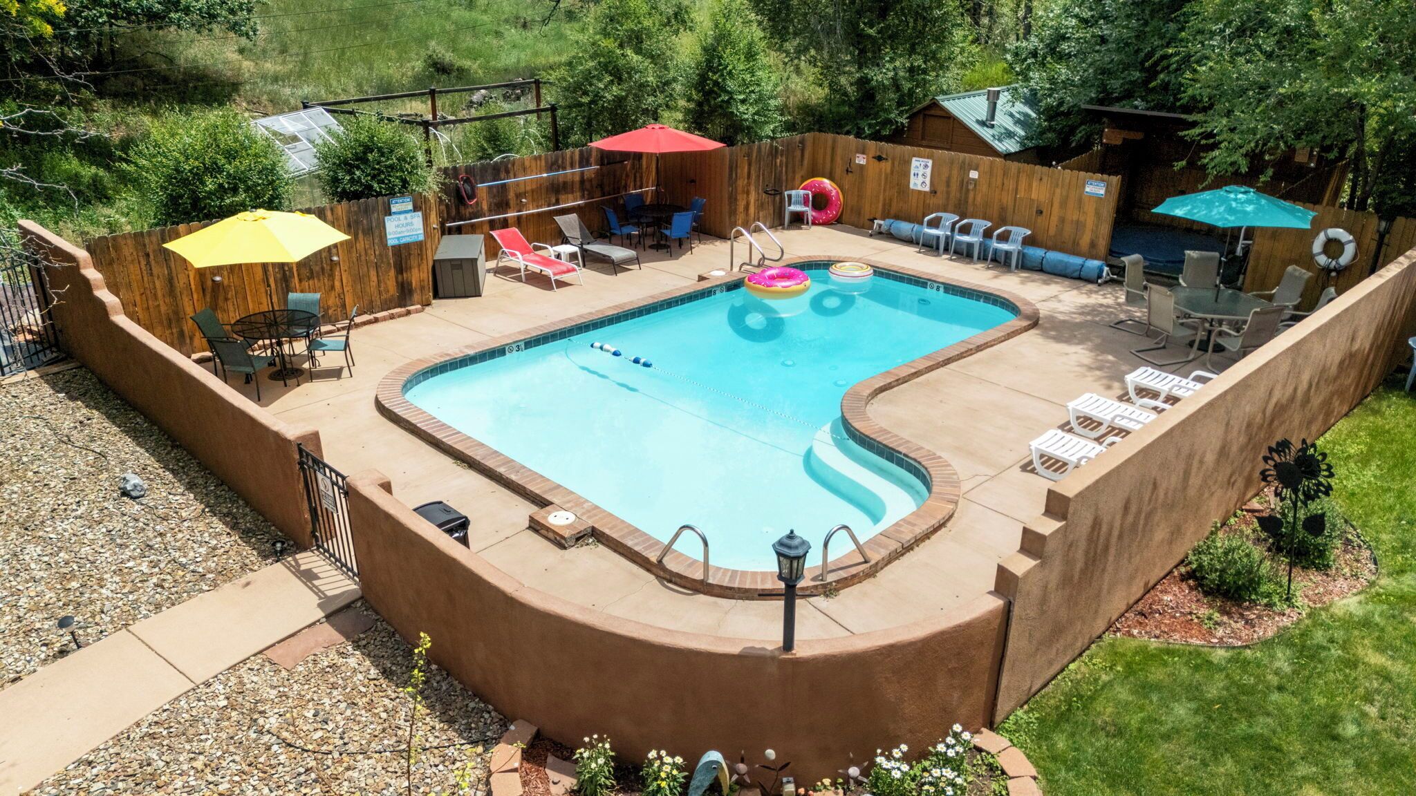A rectangular swimming pool with a wooden deck surrounding it, equipped with lounge chairs and umbrellas.