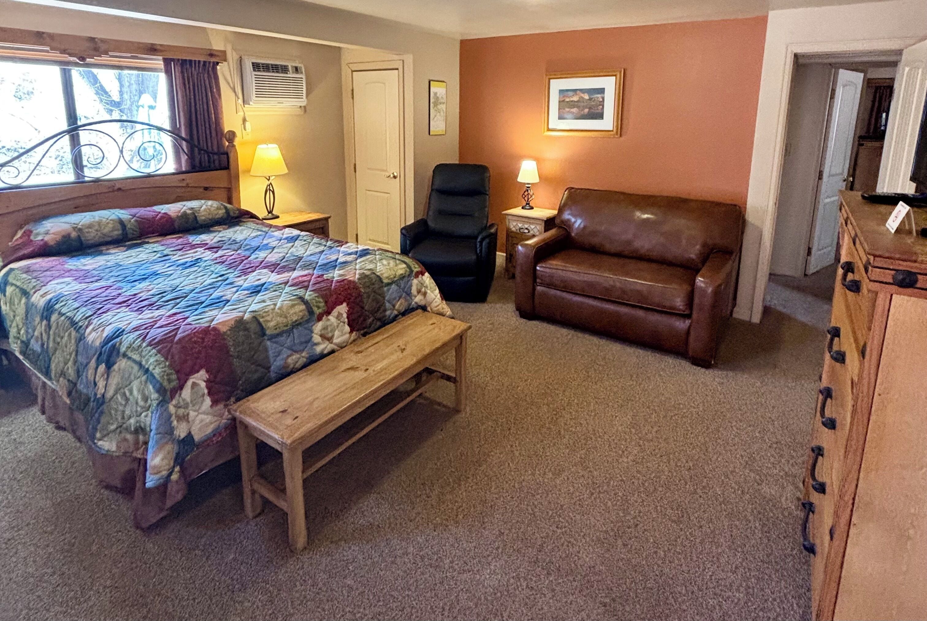 A bedroom with a bed, a chair, a bench, and a dresser.