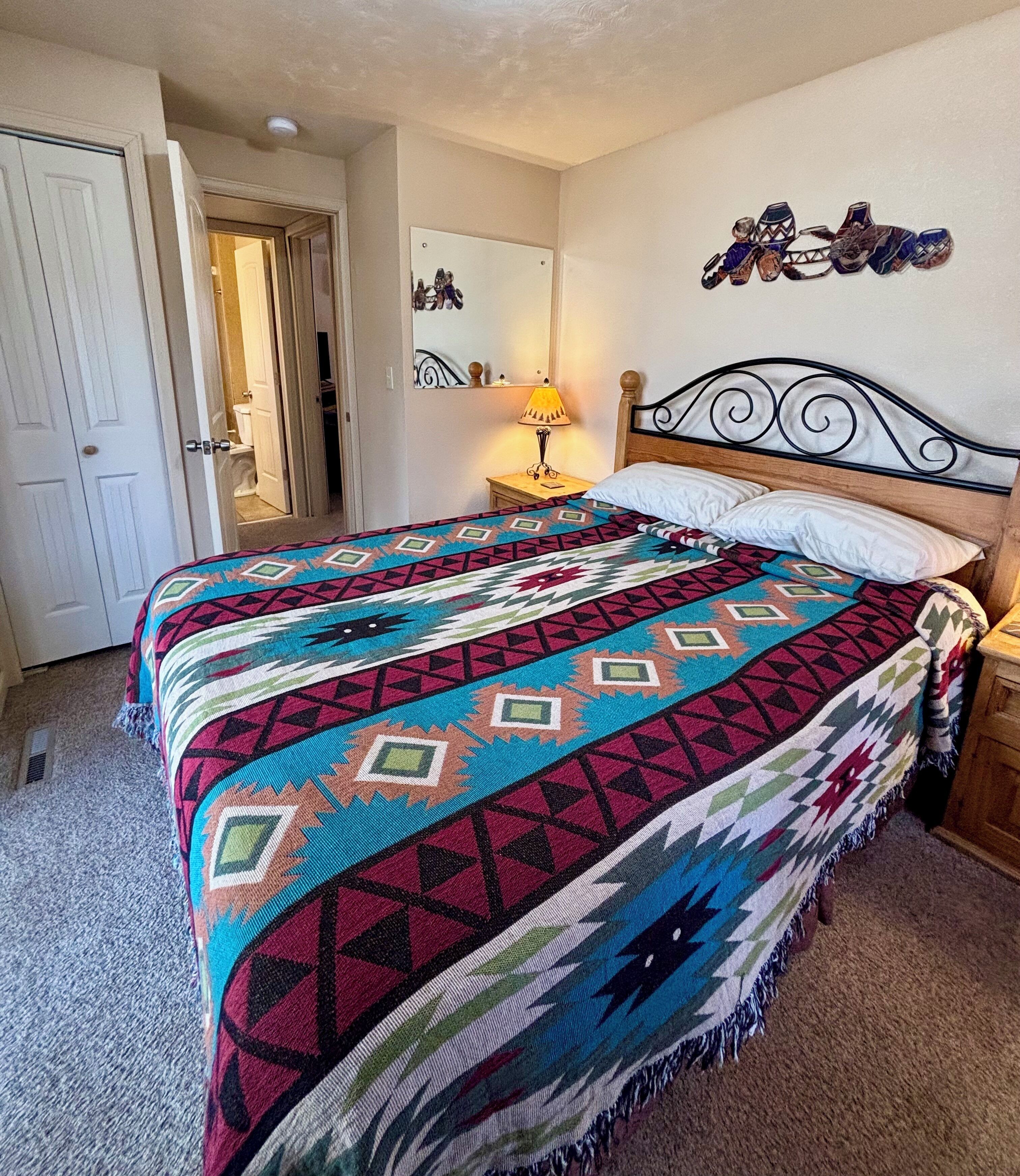 A bedroom with a bed, a nightstand, a lamp, a door, and a wall decoration.