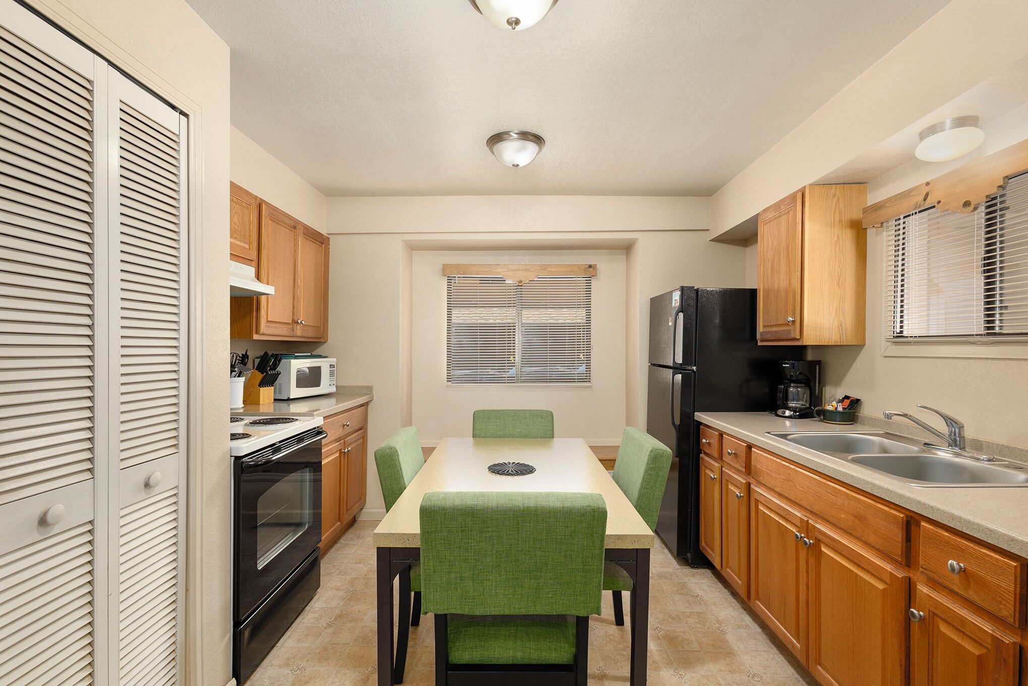 A compact kitchen with a dining table, chairs, a microwave, oven, refrigerator, and wooden cabinets.