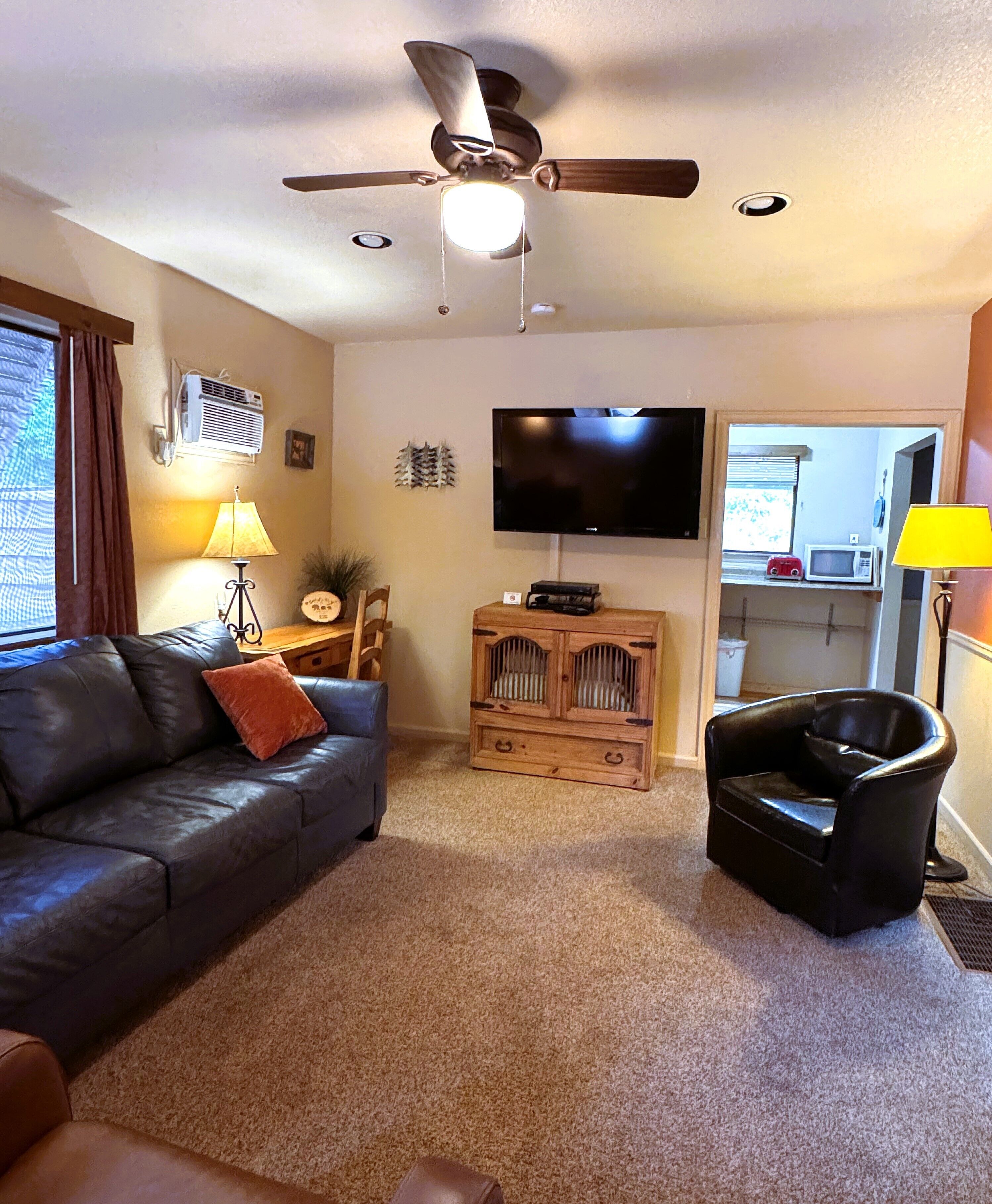 A living room with a ceiling fan, a flat-screen TV, a sofa, a chair, and a small cabinet.