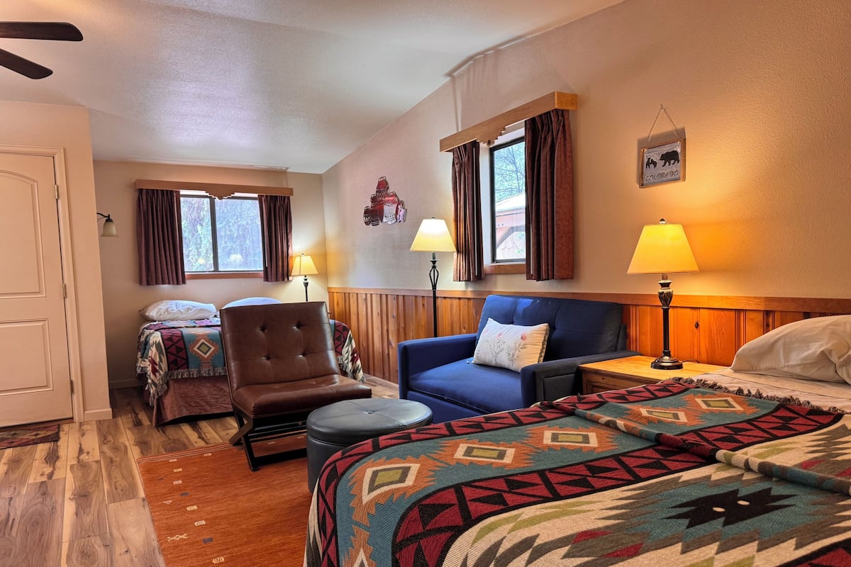 A hotel room with a bed, two sofas, a chair, a small table, and two lamps.