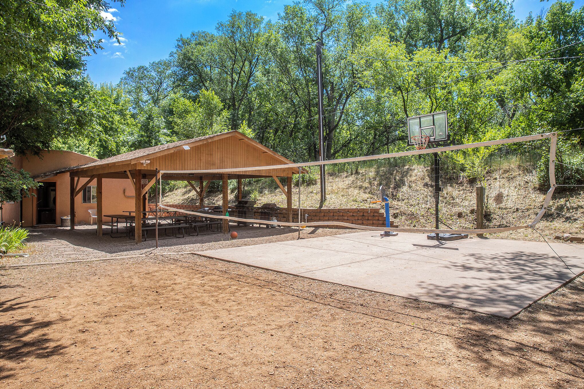 Un área de picnic techada con un aro de baloncesto, bancos de madera y una mesa de picnic.