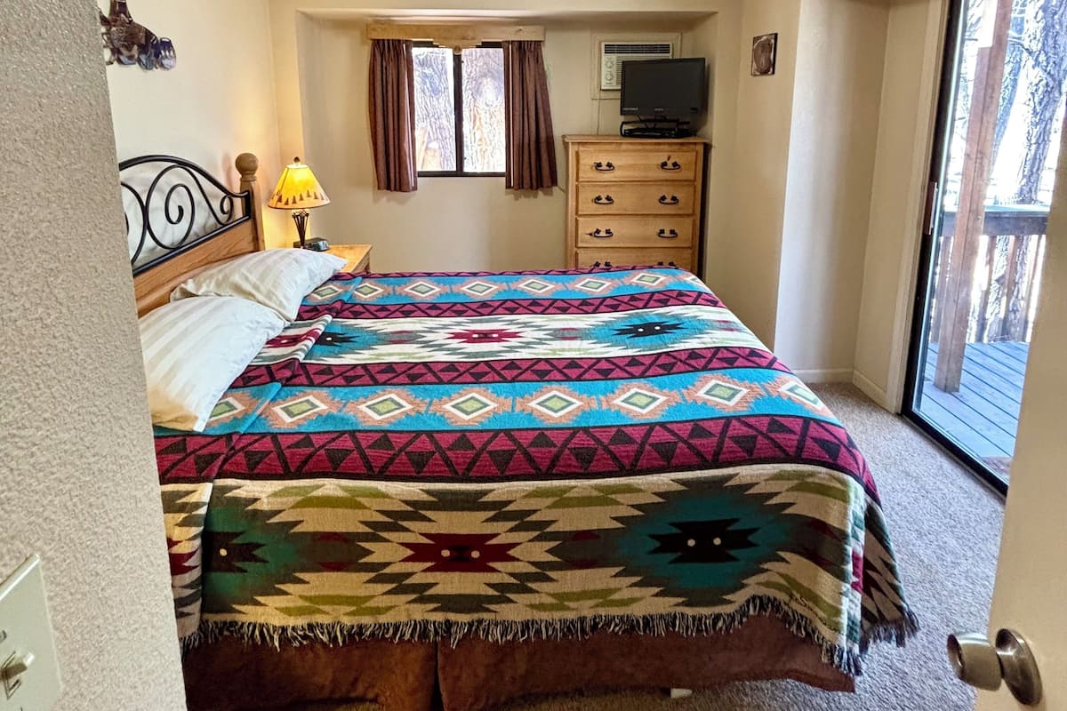 A bedroom with a bed, a dresser, a television, and a window.