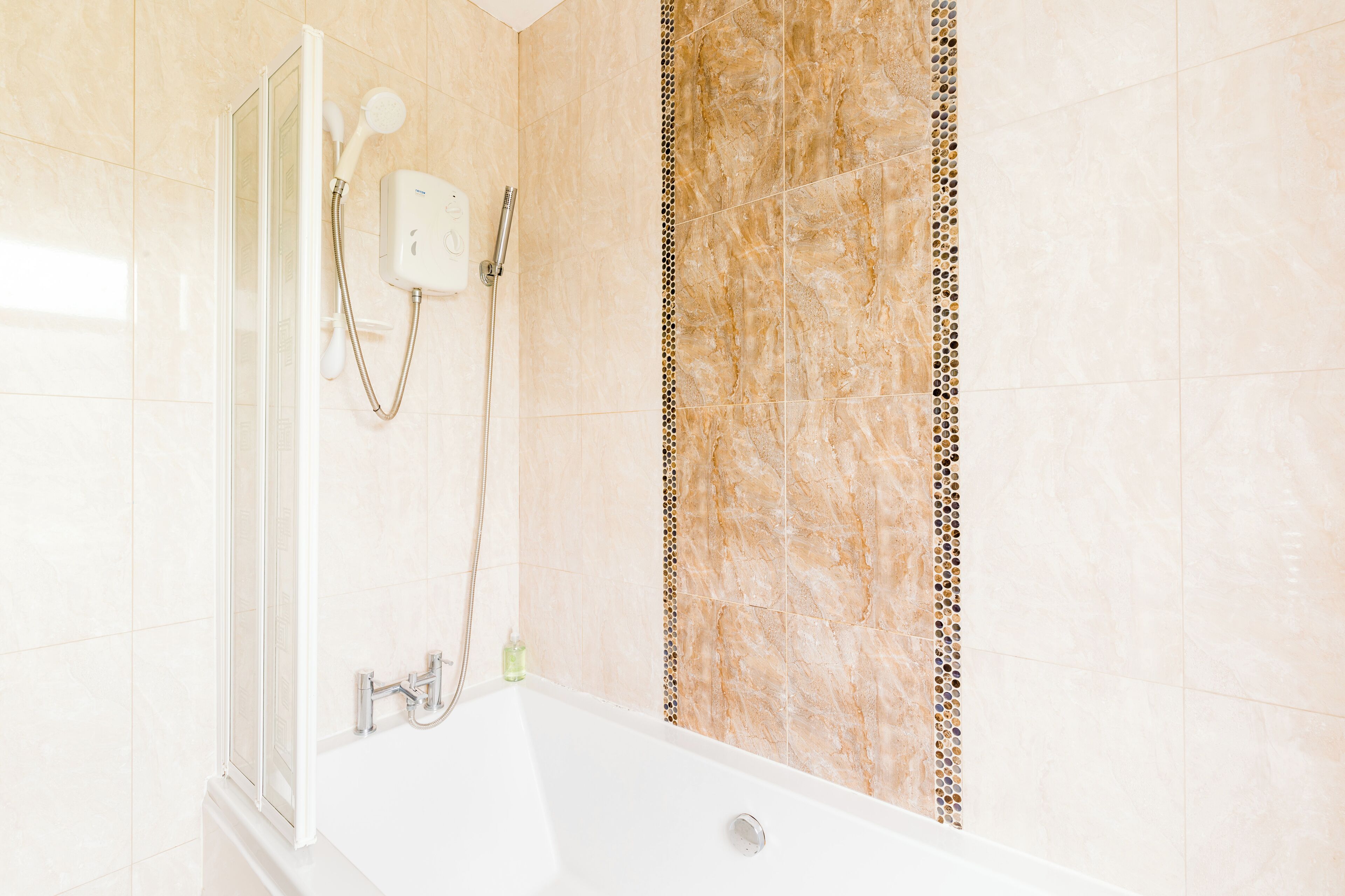 A bathroom with a bathtub, a shower, and a wall with a decorative tile border.