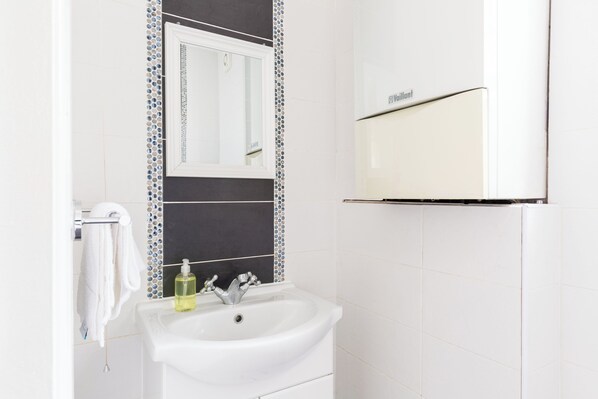 Un baño con un lavamanos blanco, un espejo y un perchero para toallas.