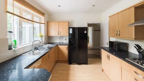 A modern kitchen with wooden cabinets, a black refrigerator, a microwave, and a sink. - 6 bedroom house near Edgbaston Stadium (Birmingham)