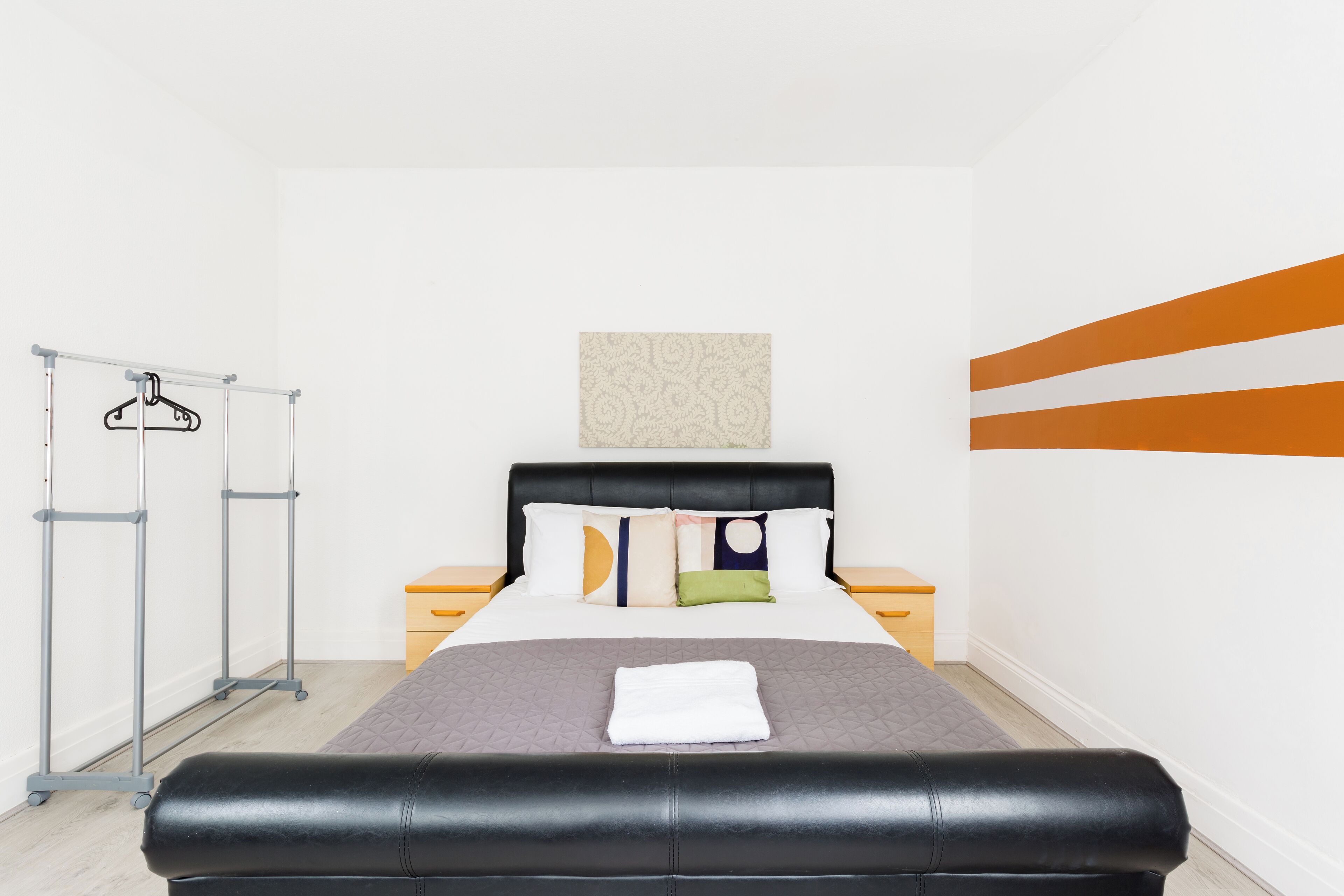 Une chambre d’hôtel comprenant un lit, une armoire, une table de chevet et un mur orné d’un motif géométrique.