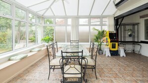 A conservatory with a glass table and chairs, a ceiling fan, and a small arcade machine. - 6 bedroom house near Edgbaston Stadium (Birmingham)
