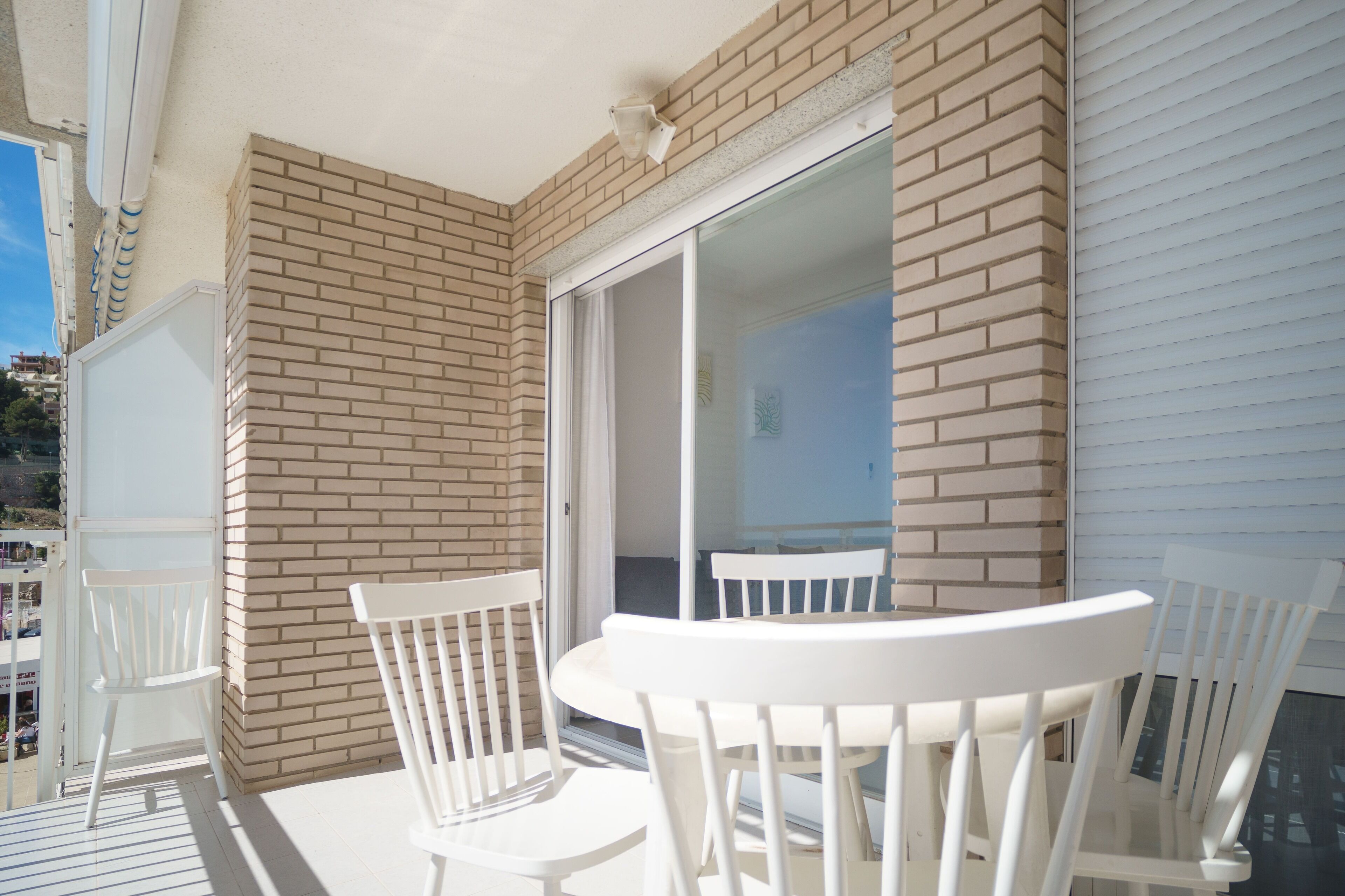 A balcony with white chairs and a table, a brick wall, and a sliding glass door.