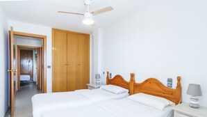A hotel room with two beds, wooden headboards, bedside tables with lamps, a ceiling fan, and a wardrobe. - Forner Apartamentos Peñiscola (Peniscola)