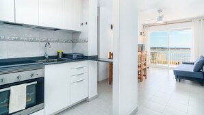 A modern kitchen with white cabinets, a stove, and a sink. There is a balcony with a view of the sea. - Forner Apartamentos Peñiscola (Peniscola)