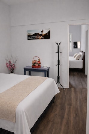 Un dormitorio con una cama, una mesita de noche con una cesta, un perchero y un cuadro en la pared.