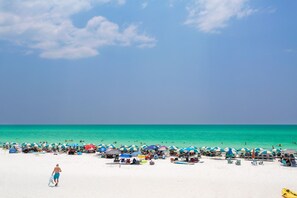 Uma praia com vários guarda-sóis e cadeiras de praia, areal e um céu azul límpido.