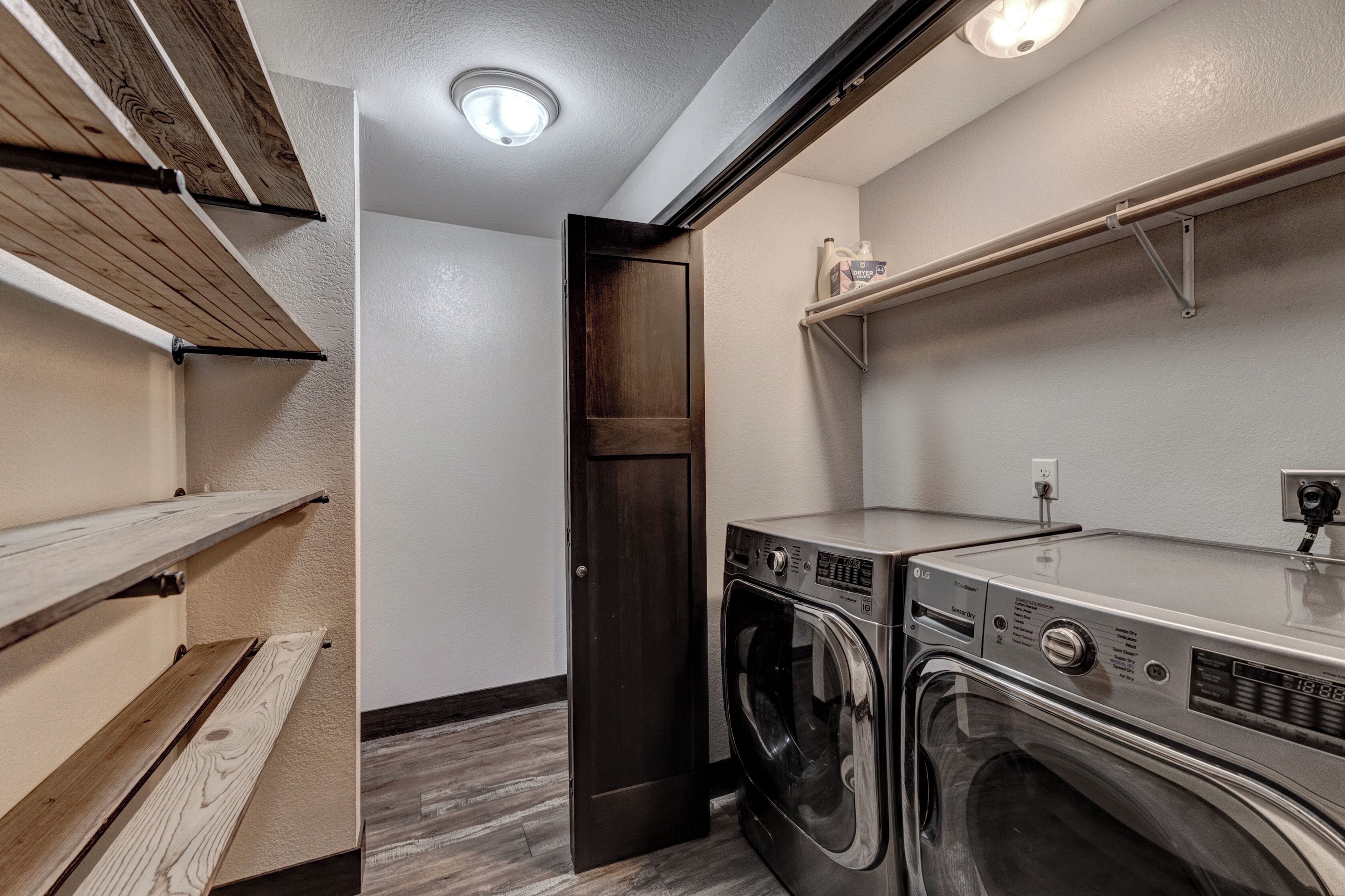 Une buanderie équipée d’un lave-linge et d’un sèche-linge, de rayonnages en bois et d’une porte.