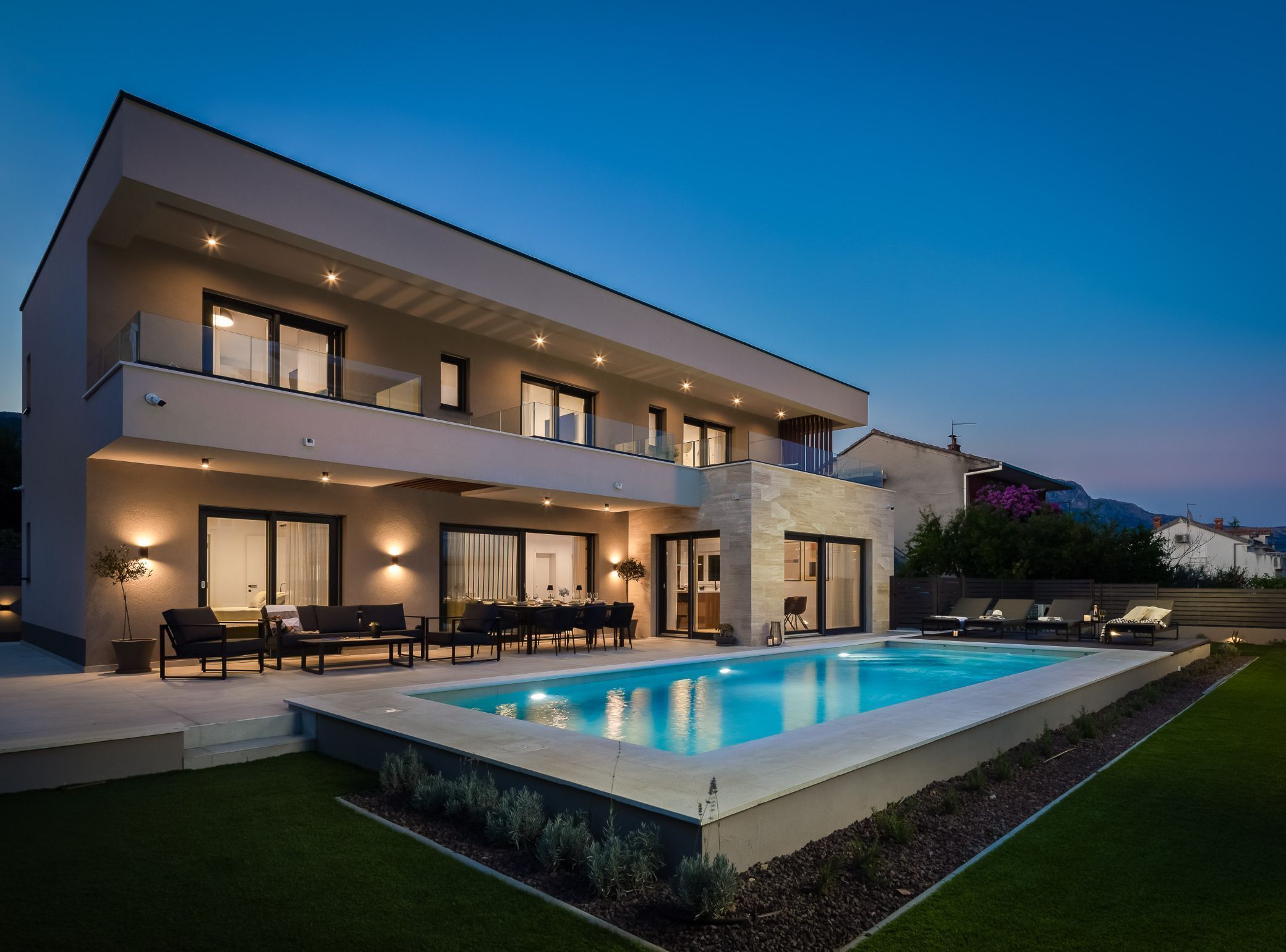 A modern two-story house with a swimming pool, outdoor seating, and a mountain view.