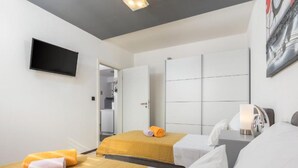 A hotel room with two beds, a flat-screen TV mounted on the wall, and a painting above the bed. - Casa Gigi (Medulin)