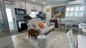 A modern kitchen with white cabinets, a microwave, and a refrigerator. There is a dining area with a white table and chairs. - Siesta Key Beach Cottage-Prime Location! Walkable. Luxury Amenities & Comfort! (Sarasota)
