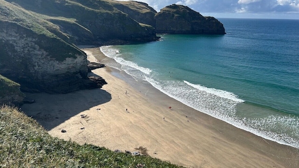 A coastal beach with cliffs, clear blue water, and a sandy shore.
