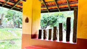 Un espacio de estar al aire libre cubierto, con una mesa de vidrio y bancos, rodeado por una estructura de madera con techo de tejas.