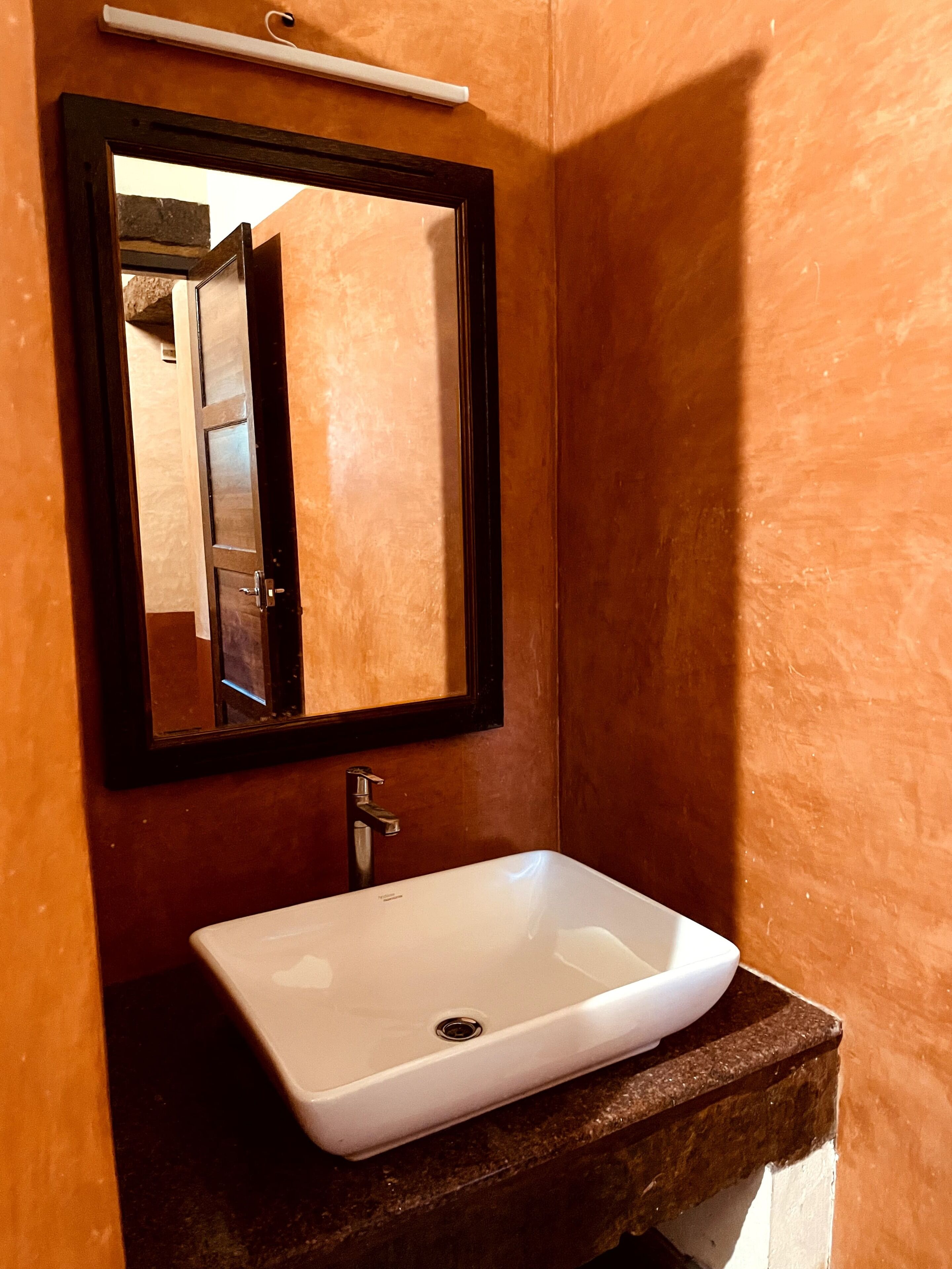 A bathroom with a white sink, a dark wooden vanity, and a mirror with a black frame.